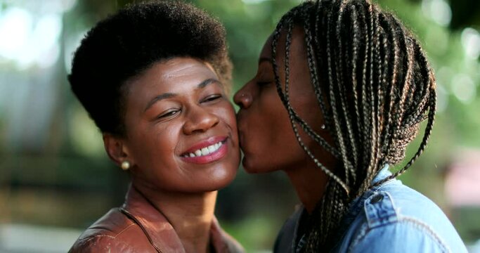 Two female friends, African women kissing friend in cheek