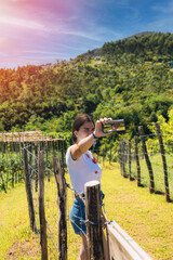 teenager with mobile phone taking a souvenir selfie on a path surrounded by hawthorn fences in the middle of the meadow and mountains full of vegetation on a sunny