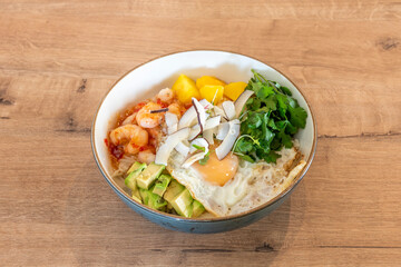 Bowl of prawns and fried egg with pieces of coconut, coriander, chopped mango and avocados with a white rice base