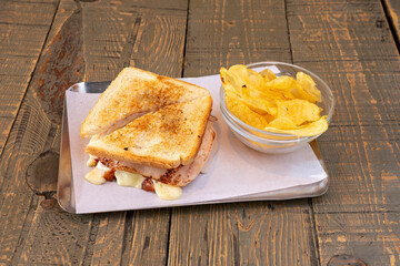 Mixed sandwich with toasted sliced bread, grilled ham and melted cheese dripping around the edges with fried potatoes.