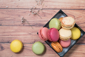 french dessert macarons of different colours and dry flowers on a wooden background 