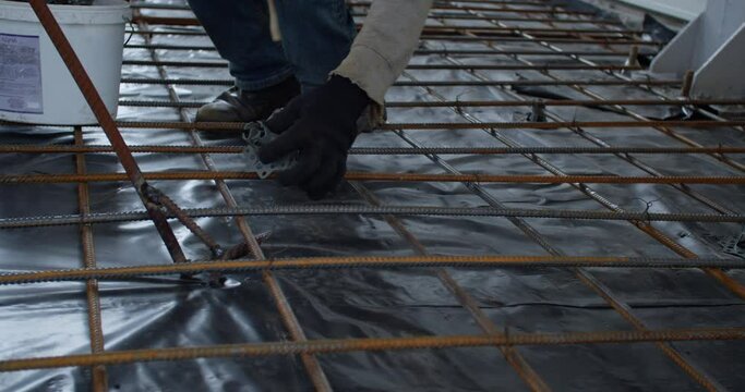 Two people are preparing the metal rods for pouring of concrete, putting spacers