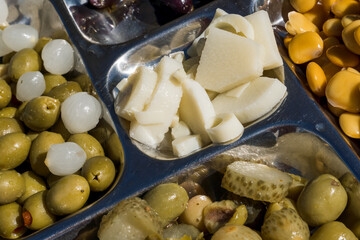 Metal platter with some traditional Brazilian snacks. Stoneless green olives, pickles, lupine, heart of palm, chives and black olives.