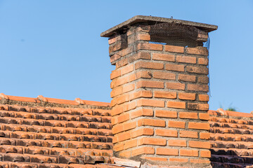 Roof with tiles and red chimney in the interior of Brazil. In the background trees and blue sky.