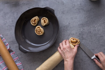 White mid woman slicing a complete cinnamon roll and deploying the pieces in a rustic ceramic tray.