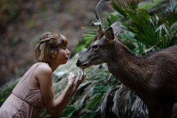 Young beautiful elegant woman with a deer in a forest. Natural wildlife conservation park.