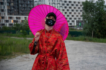 Positive man wit dressed in street style clothes red kimono with chains around neck, black cap and black medical mask . Youth and lifestyle concept. polluted city air