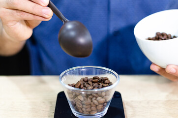 Weighing coffee grains on digital scale. Hands of male barista pouring roasted coffee grains on a