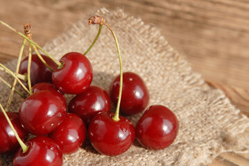 Some large ripe juicy fresh cherries on a burlap cloth on a wooden table. Tasty vitamins. Harvesting. Macro.
