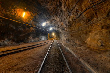 Tunnel of the mining of an underground mine. Lots of pipelines on the ceiling and rail track for trolleys