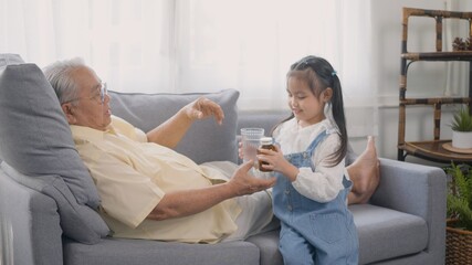 Asian granddaughter brought medicine and water for Grandpa to eat on the sofa in the lounge, Senior old man taking pills medicine time, granddaughter take care older with love