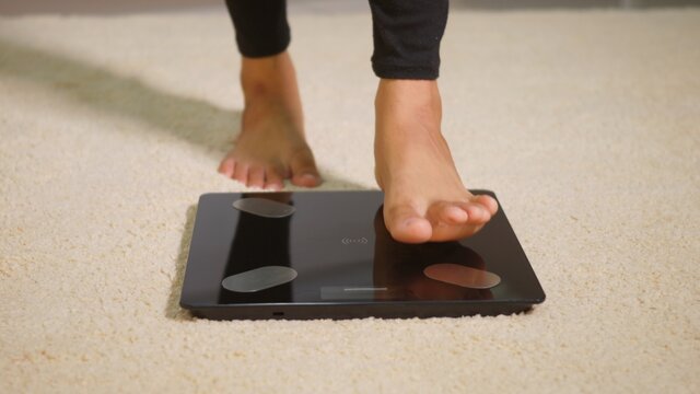 Asian Young Woman Leg Stepping Standing On Floor Electric Scales, Female Working Out At Home In Living Room, Female Stand On Digital Weighing Machine. Healthy Weight Loss Control Concept, Slow Motion