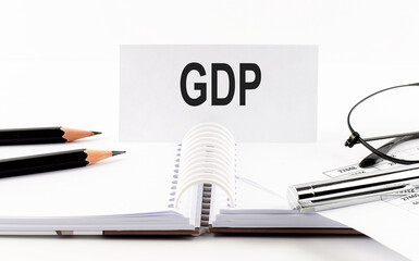 Text GDP on paper card,pen, pencils, glasses,financial documentation on table - business concept