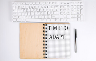 TIME TO ADAPT text on the notebook with keyboard on white background