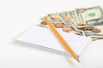 Wooden pencil on a small striped notebook with coins and money