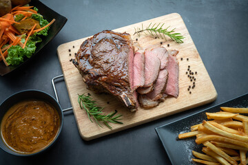 Close-up view of Grilled marble Rib eye steak beef for steak on wooden plate with salad and French fries.
