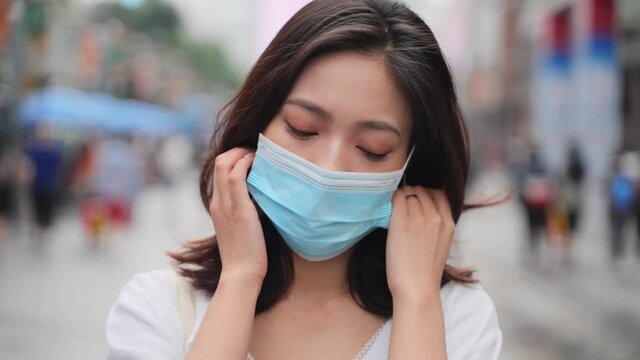 asian woman take off mask looking at camera smile in the urban asian street  The epidemic of Covid-19 is over happy people remove mask enjoy the life