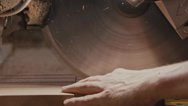 Carpentry works - worker slowly cutting along the wooden detail with a big circular saw in small pieces