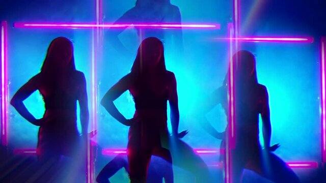 Silhouette of sexy woman dancing on glowing square of led red lamps background. She looks seductively. Sexy outfit . Kaleidoscope effect. Blue smoky studio.