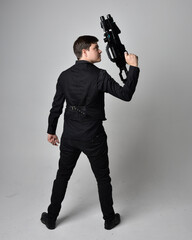 Full length portrait of a  brunette man wearing leather jacket  and holding a science fiction gun. ...