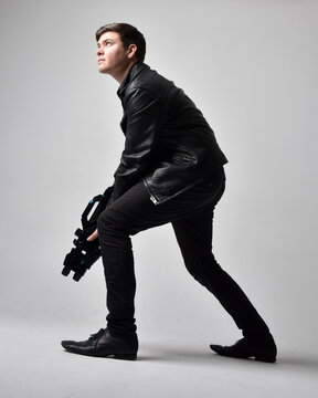 Full length portrait of a  brunette man wearing leather jacket  and holding a science fiction gun.  Standing  action pose isolated  against a grey studio background.