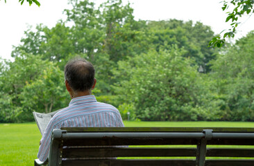 Middle-aged and older or elderly reading a newspaper on a park bench....