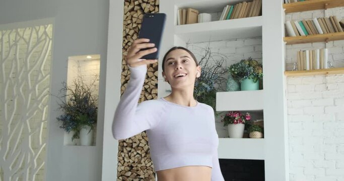 Trendy happy woman vlogger dances and recording videostream video for social media. Enjoyed female taking selfies using smartphone. Creating dancing video using tiktok app.