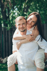 Fototapeta premium the love of a young husband and wife, happy faces, a date in nature, joy, a guy rides a girl on his back. Love forever Romance young