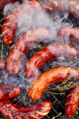 BBQ pork sausage with thyme while grilling on a cast iron grill, top view