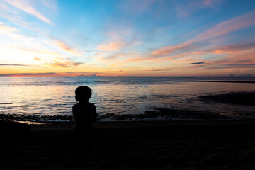 the boy silhouette on a sea beach at sunrise, kid and sea
