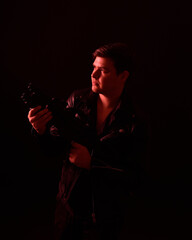 Obraz na płótnie Canvas close up portrait of a brunette man wearing leather jacket and holding a science fiction gun. Standing action pose with red silhouetted lighting against a black studio background.