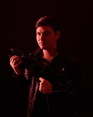 Fototapeta na wymiar close up portrait of a brunette man wearing leather jacket and holding a science fiction gun. Standing action pose with red silhouetted lighting against a black studio background.