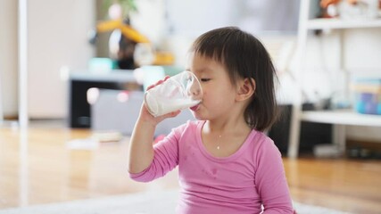 close up of lovely asian baby girl holding glass of milk drinking at home baby growth concept