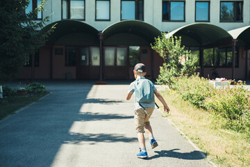 The boy, elementary school student, walking to school with bag behind back and book. Students are ready for the new year. Back to school.