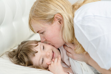 Obraz na płótnie Canvas Mom kissing a girl with down syndrome in the bedroom on the bed while going to bed. Ordinary childcare in a family for children with disabilities