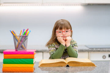 A girl with down syndrome reading a book at home and smiling while looking at the camera. Family education for children with disabilities