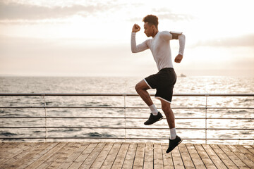 Strong young curly dark-skinned man in black sport shorts and long-sleeved t-shirt jumps and runs...