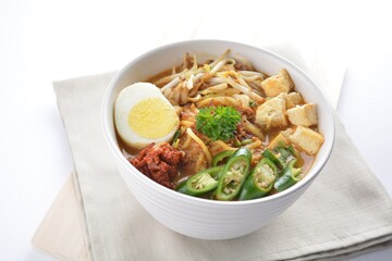 Malay mee rebus noodle with boiled egg, tofu, green chilli, sambal chilli sauce and hot thick curry gravy soup bowl in white background asian halal menu