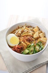 Malay mee rebus noodle with boiled egg, tofu, green chilli, sambal chilli sauce and hot thick curry gravy soup bowl in white background asian halal menu