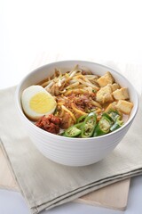 Malay mee rebus noodle with boiled egg, tofu, green chilli, sambal chilli sauce and hot thick curry gravy soup bowl in white background asian halal menu