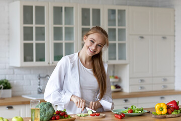 Beautiful happy woman in the kitchen preparing vegetable salad smiling looking at the camera.