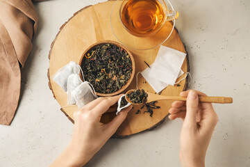 Woman putting dry tea leaves in bags on light background