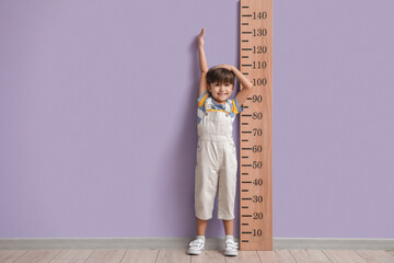 Little boy measuring height near color wall