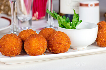 Meat balls fried with cheese filling, close-up, on a plate. Near the wine glasses and a bottle of wine and napkins.