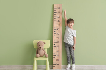 Little boy measuring height near color wall