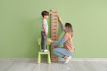 Woman measuring height of her little son near color wall