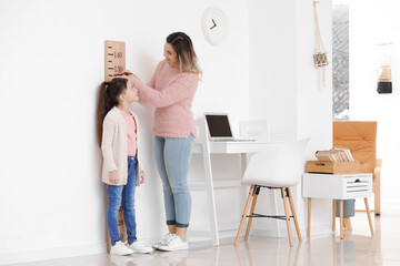 Woman measuring height of her little daughter at home