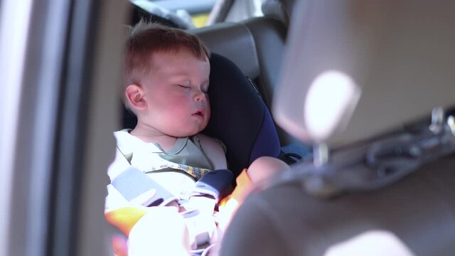little boy asleep napping or sleeping in a car seat in very hot sunny weather