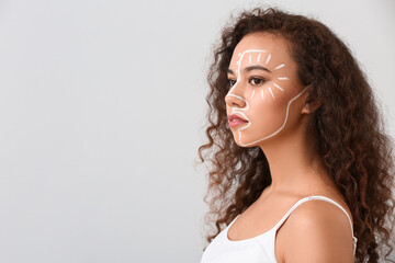 Beautiful young African-American woman with paint on her face against light background