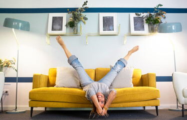 Happy and joyful adult woman lay down on the sofa in reverse position with legs up and head down...